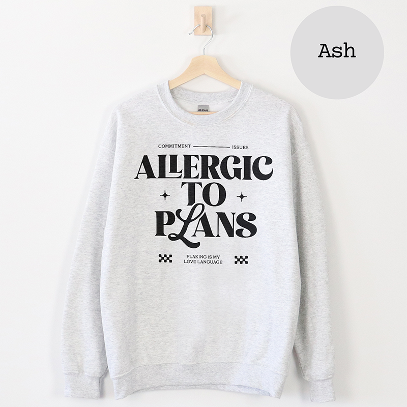 Flat lay of the Allergic to Plans sweatshirt in ash grey, unisex fit with bold black text — cozy and minimal design.