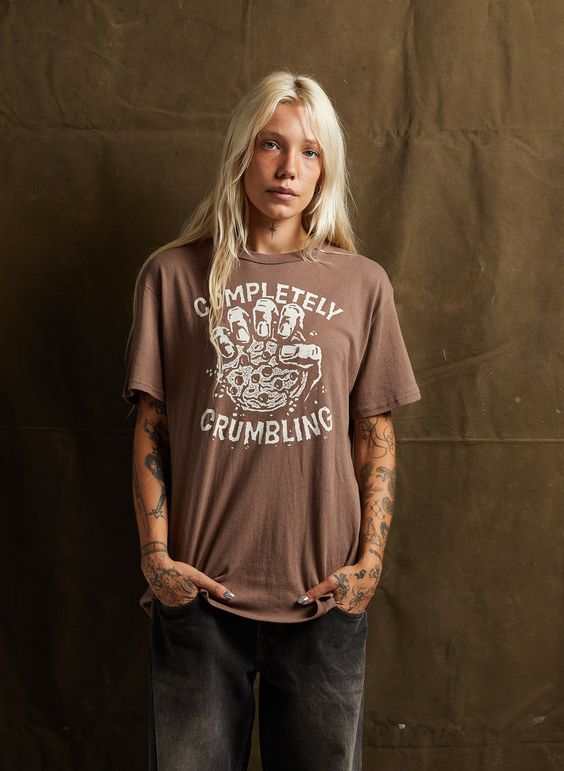 Female model in black jeans wearing the Completely Crumbling unisex tee with cookie graphic. Relaxed and casual style.