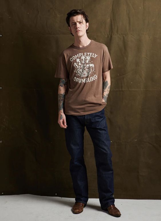 Male model wearing the Completely Crumbling tee with denim and boots. Unisex Pyknic shirt featuring cookie graphic.