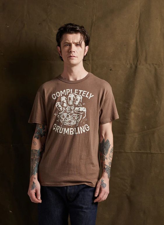 Man in jeans modeling Pyknic’s Completely Crumbling tee. Features cookie graphic and relaxed, casual fit.