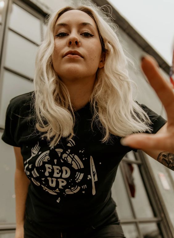 Close-up of blonde model leaning toward camera in Fed Up graphic tee. Broken plate design on soft black cotton shirt.