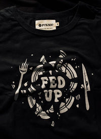 Flatlay of Fed Up graphic tee on black background. Broken plate design and bold lettering centered on black shirt.