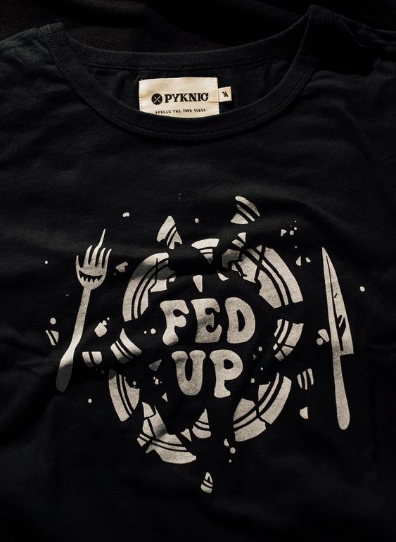 Flatlay of Fed Up graphic tee on black background. Broken plate design and bold lettering centered on black shirt.