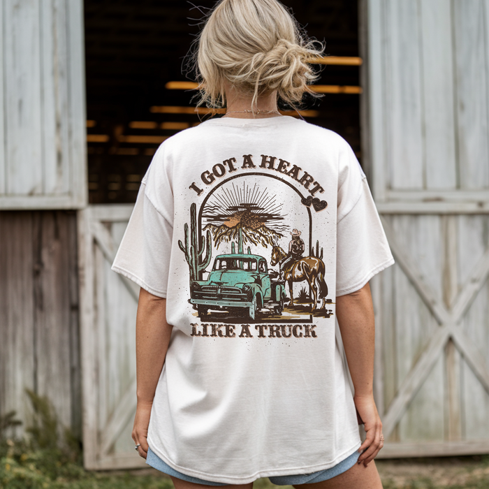 Back view of model wearing Heart Like a Truck tee in front of barn — white western graphic tee for women