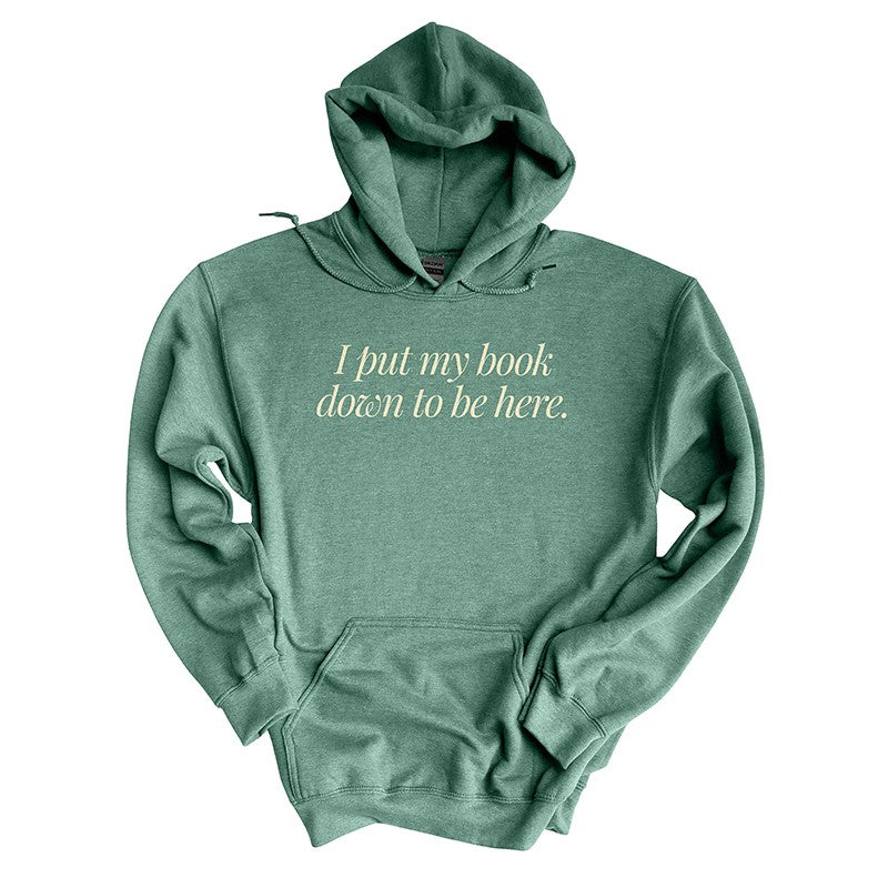Flat lay of heather dark green “I Put My Book Down To Be Here” hoodie – funny reading hoodie for bookworms
