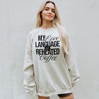 Woman wearing oversized My Love Language Is Reheated Coffee sweatshirt in heather dust (Bella Canvas style) with biker shorts — relaxed and comfy look.