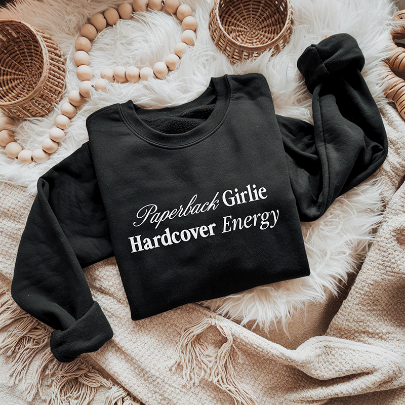Flat lay of the Paperback Girlie Hardcover Energy sweatshirt in black (Bella Canvas style) — bold bookish graphic on ultra-soft fleece.

