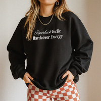 Woman wearing the Paperback Girlie Hardcover Energy sweatshirt (Gildan style) with clay-colored checkered pants — cozy reader aesthetic.
