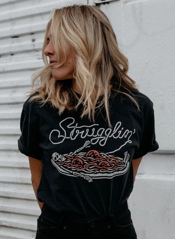 Close-up of blonde woman wearing the Strugglin’ skeleton pasta tee. Graphic and soft cotton texture.