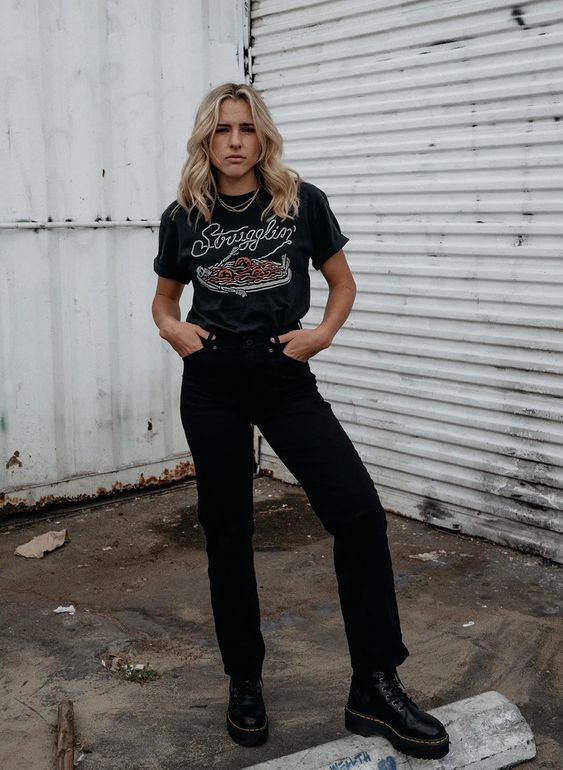 Blonde model wearing Strugglin’ tee with black pants and boots. Full body photo showing relaxed, casual style.