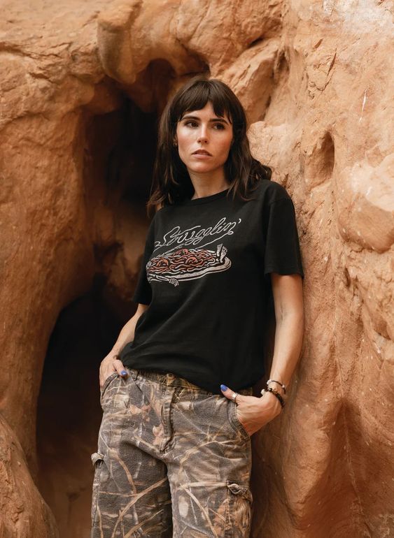 Model with dark hair in camo pants wearing Strugglin’ tee in front of red rocks. Nature backdrop with edgy outfit.